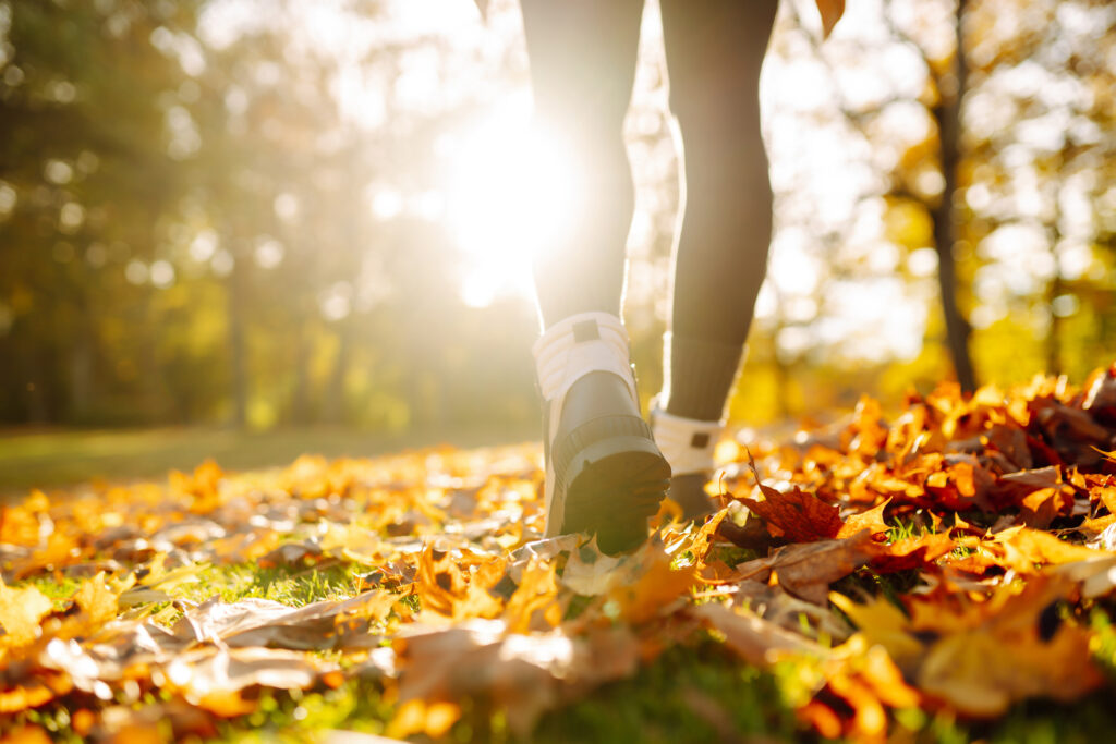 Close-up of female legs in hiking boots walks on ground with yellow-orange dry fall leaves during autumn season in park or forest